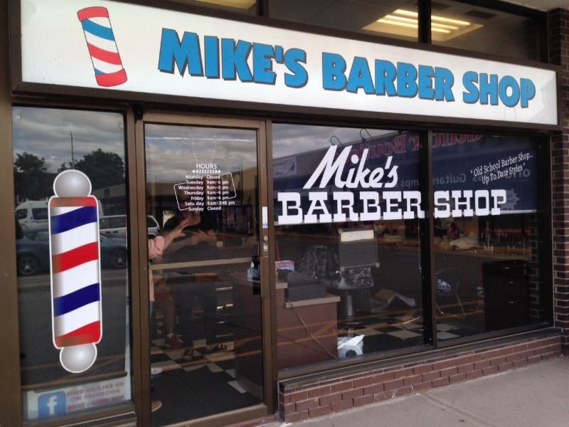 Storefront of Mike's Barber Shop with barber poles and signage at Town Plaza, Whitby